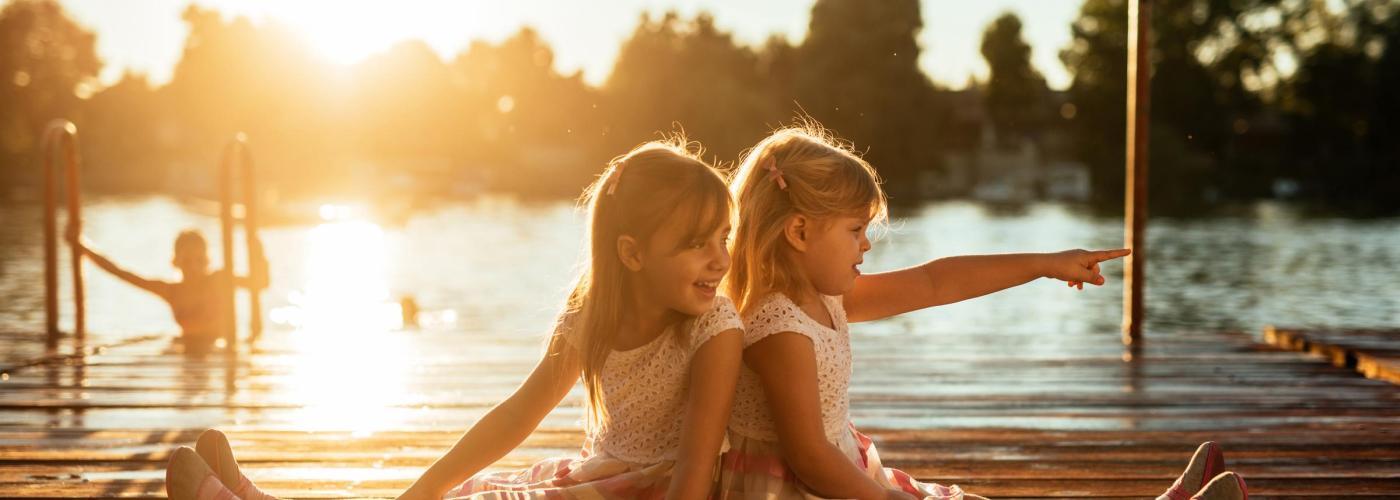 Two girls sitting on a dock, pointing to the right.