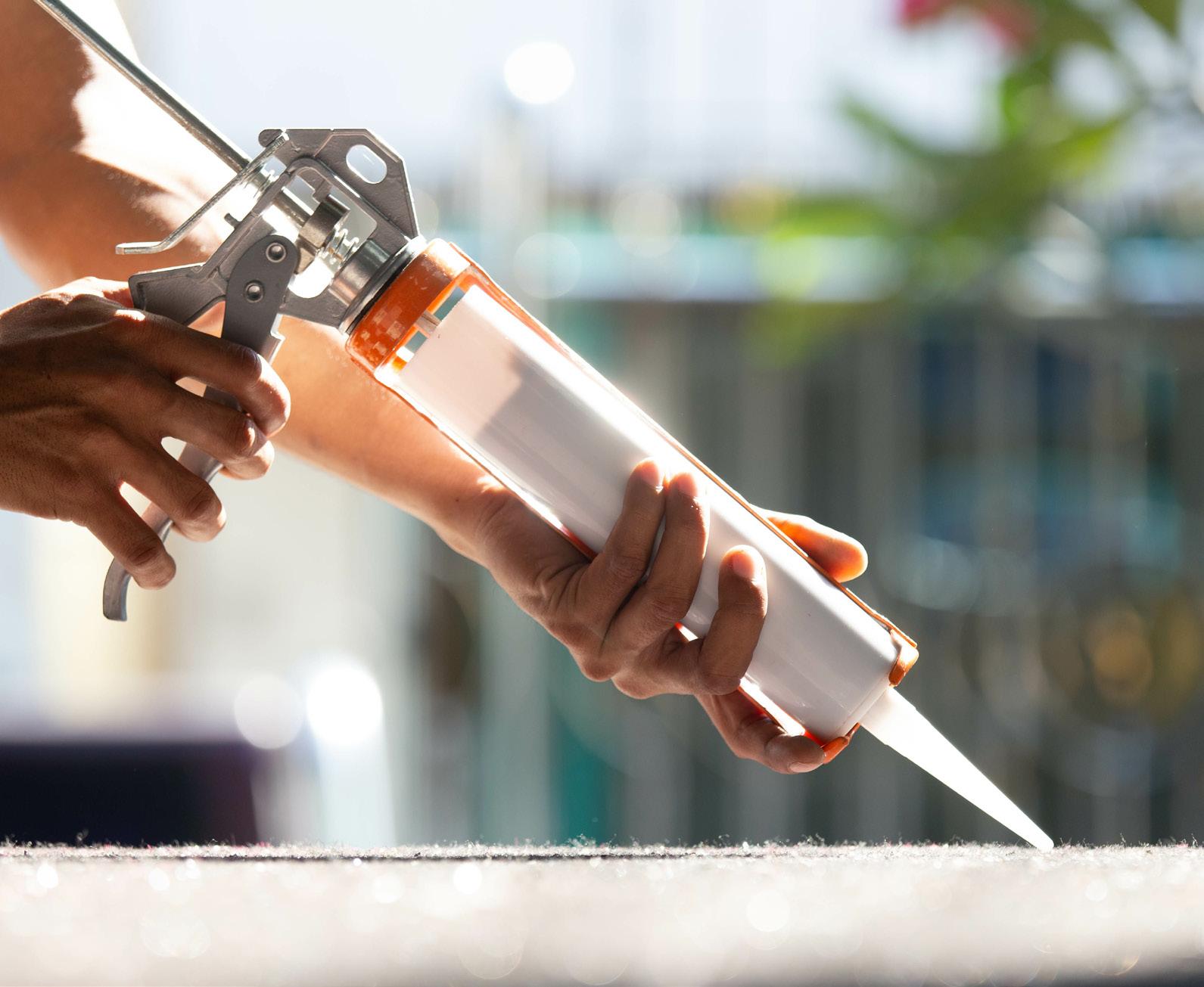 Woman applying caulk to a railing outside.